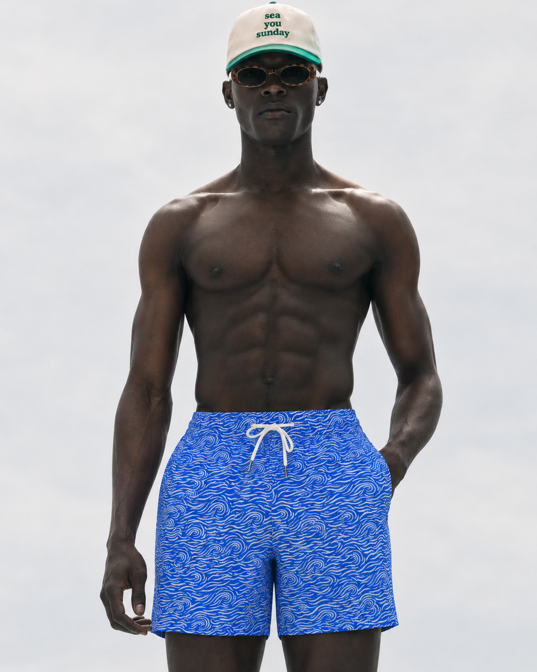 Man wearing blue swim shorts with a white cap and sunglasses on a light gray background