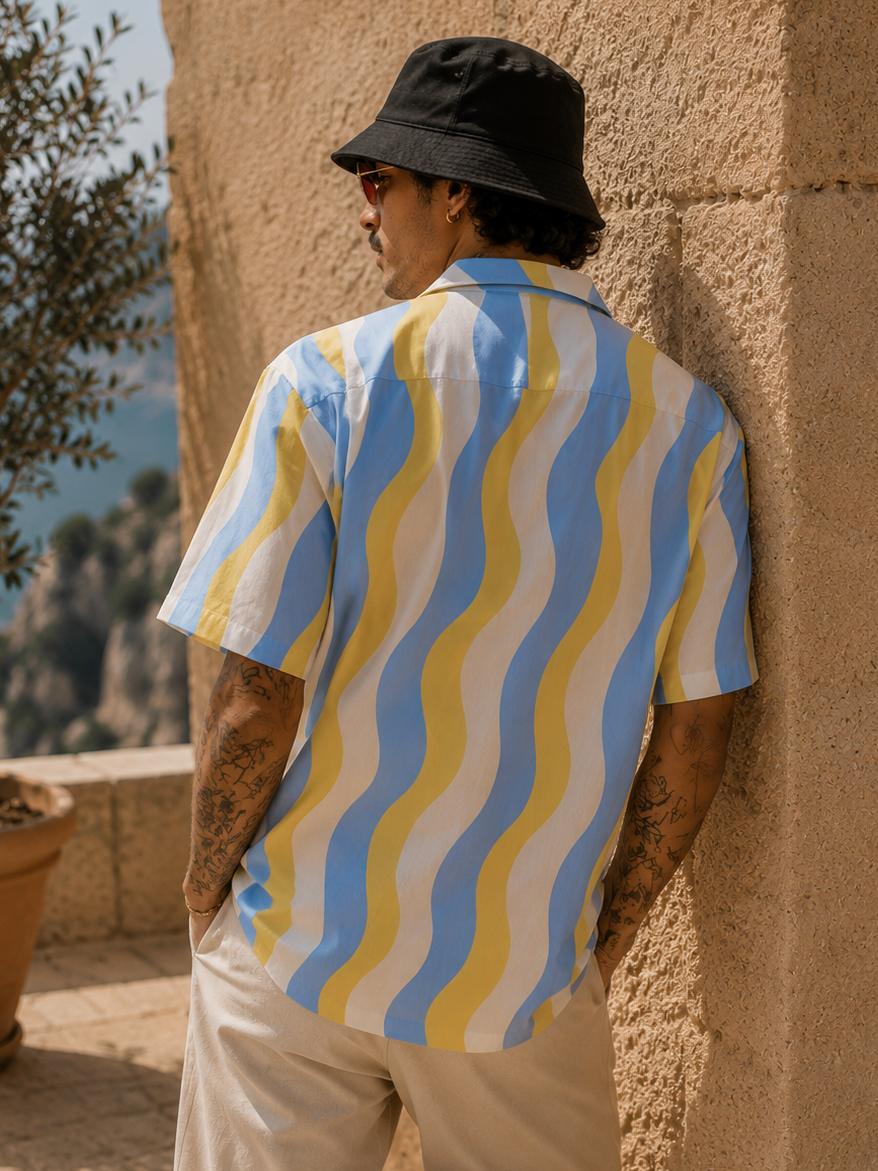 Person wearing a colorful shirt leaning against a stone wall with a scenic background.