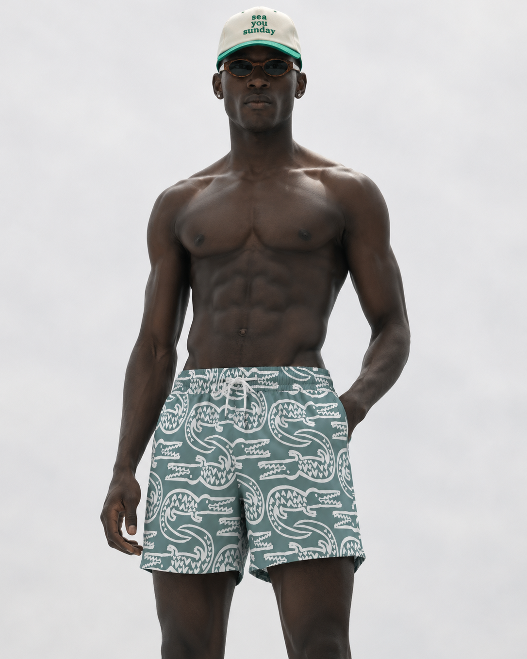 Man wearing patterned swim shorts and a cap on a plain background