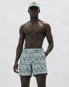 Man wearing patterned swim shorts and a cap on a plain background