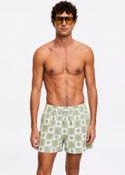 Man wearing green checkered swim shorts and sunglasses on a white background