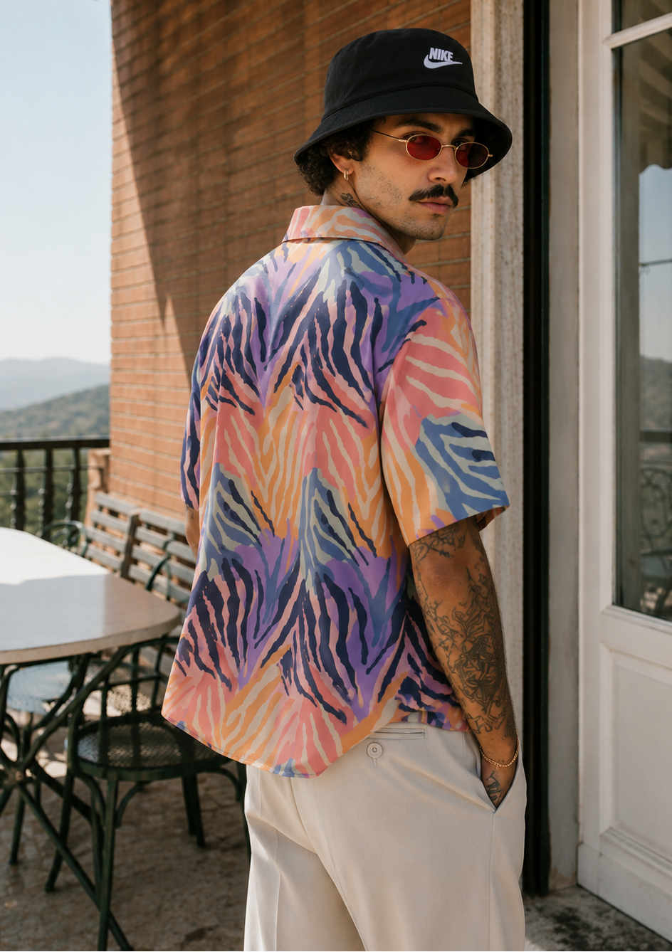 Man wearing a colorful shirt and black bucket hat standing on a porch.
