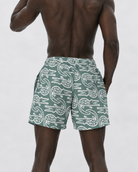 Man wearing green swim shorts with white patterns on a plain background