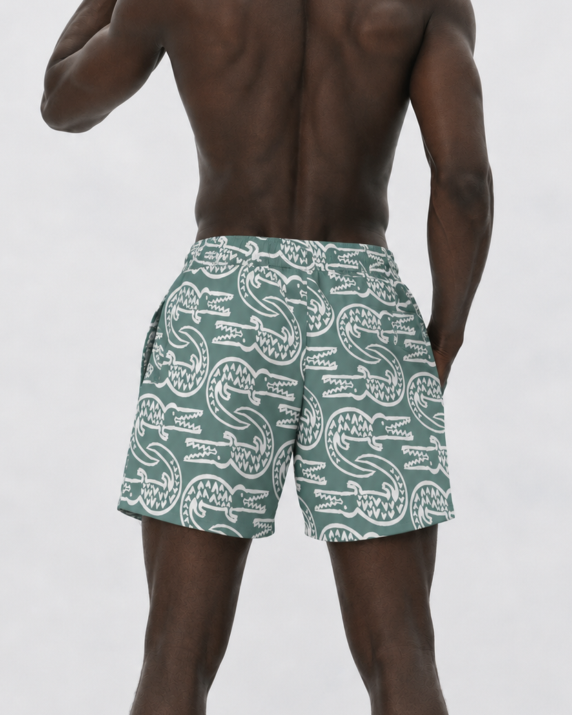 Man wearing green swim shorts with white patterns on a plain background