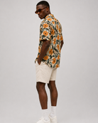 Man wearing a floral shirt, beige shorts, and white sneakers on a gray background