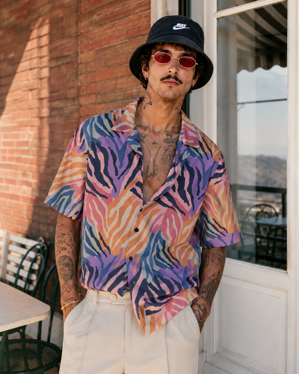 Man wearing a colorful shirt and black bucket hat standing in front of a building.
