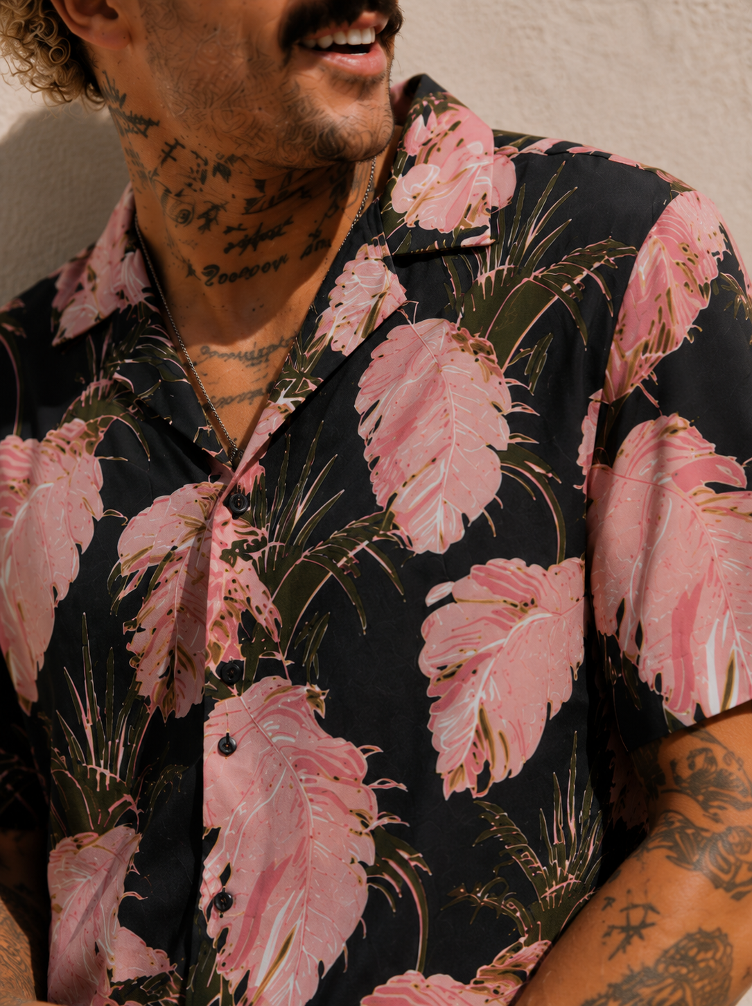 Man wearing a black floral shirt with pink flowers against a neutral background