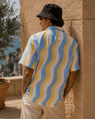 Person wearing a colorful shirt leaning against a stone wall with a scenic background.